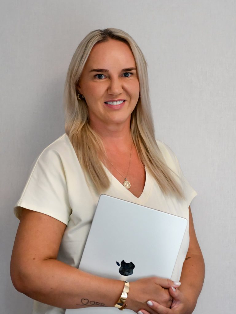 Kasia Kraszewska - Uśmiechnięta kobieta z długimi blond włosami trzymająca zamknięty laptop.